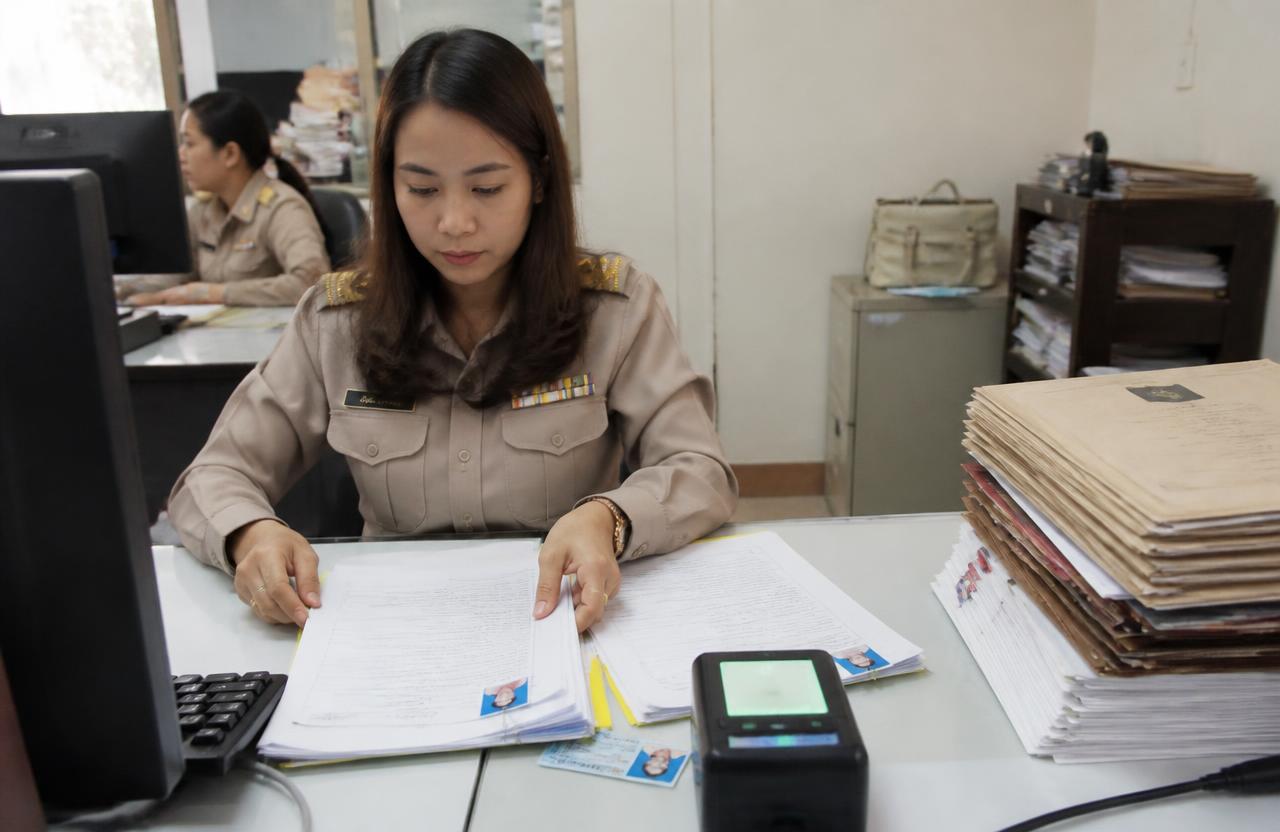 เจ้าหน้าที่กำลังตรวจแบบฟอร์มขึ้นทะเบียนประกันสังคมของลูกจ้างพร้อมแฟ้มเอกสารบนโต๊ะทำงาน